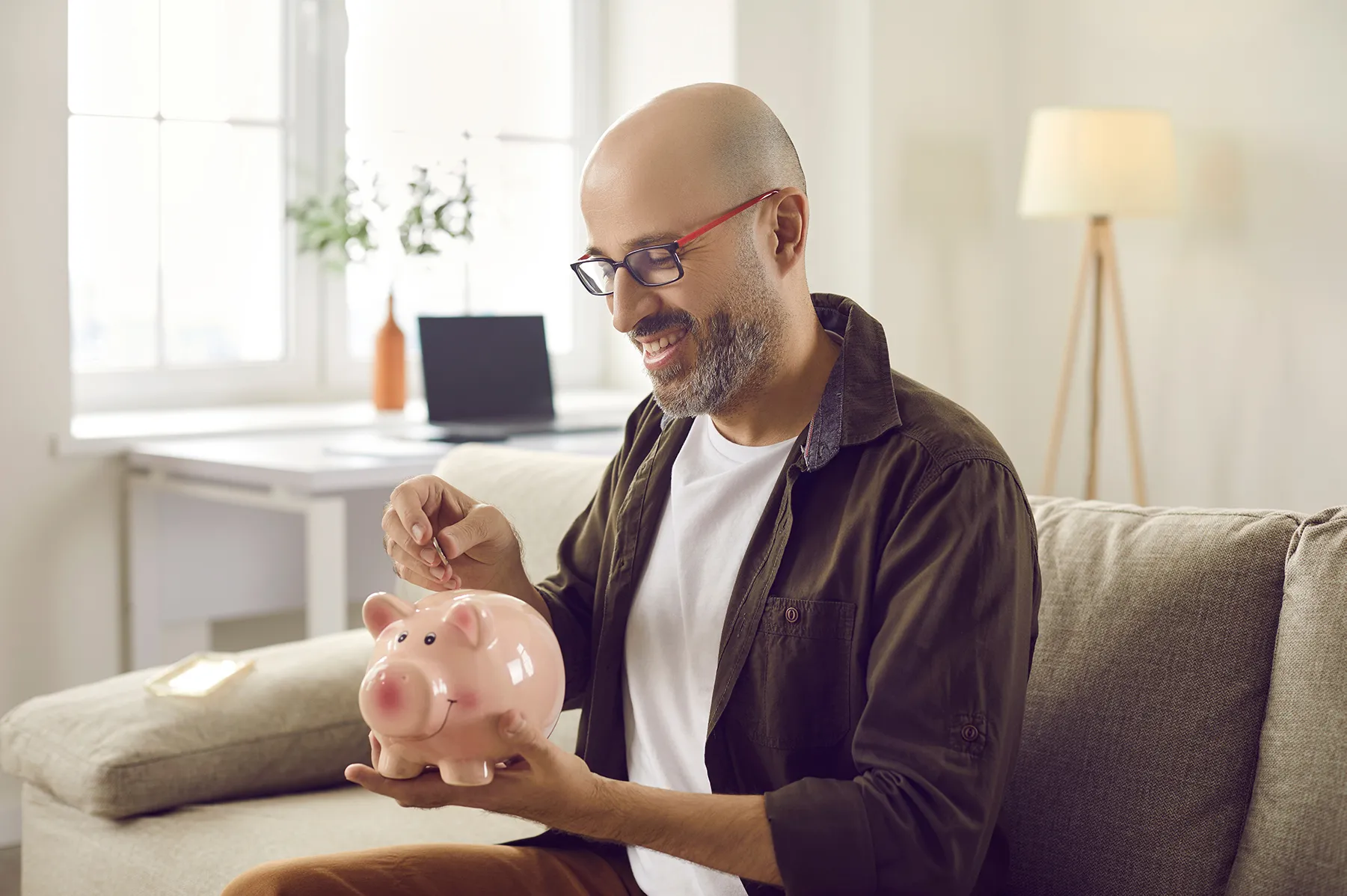 man sitting on a couch putting a coin into a piggybank