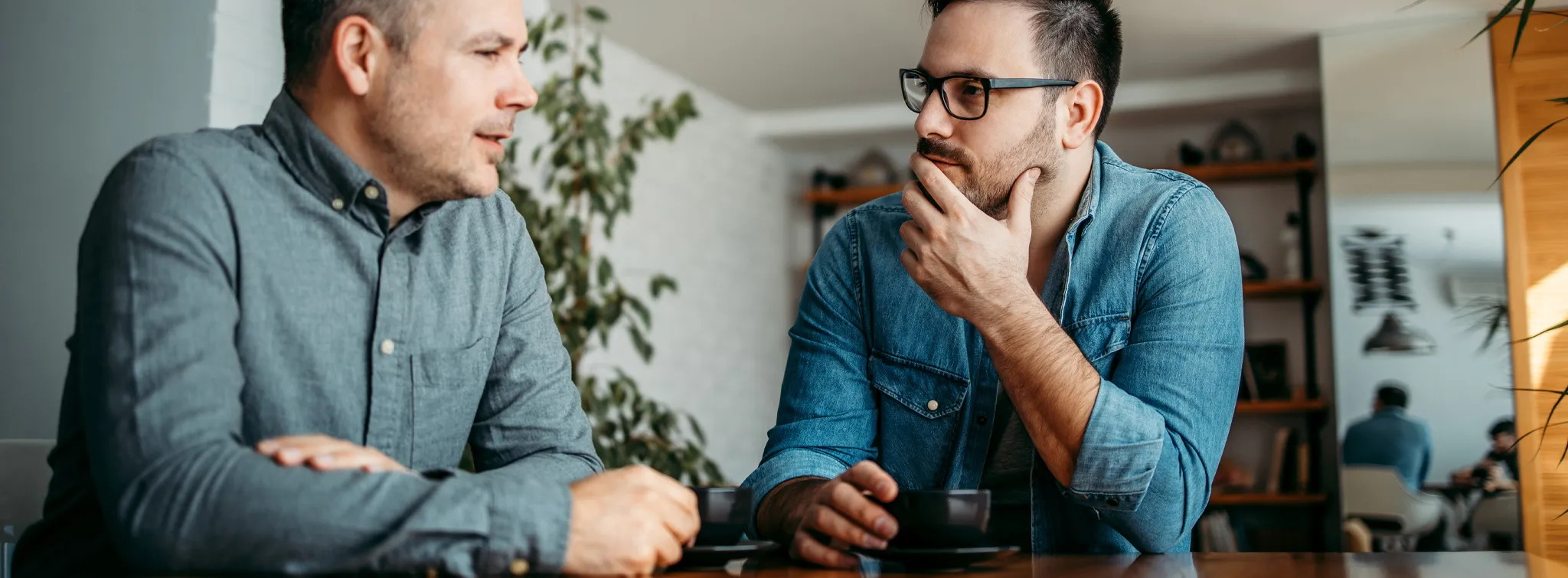 two men sitting at a table discussing over coffee