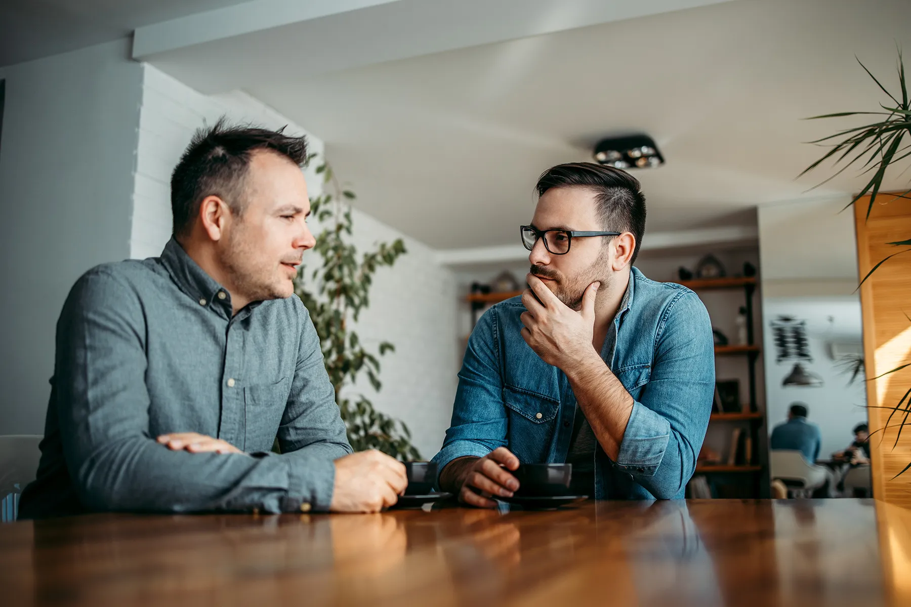 two men sitting at a table discussing over coffee