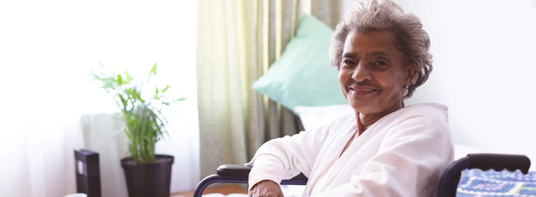 elderly woman sitting in a wheelchair near a window and smiling