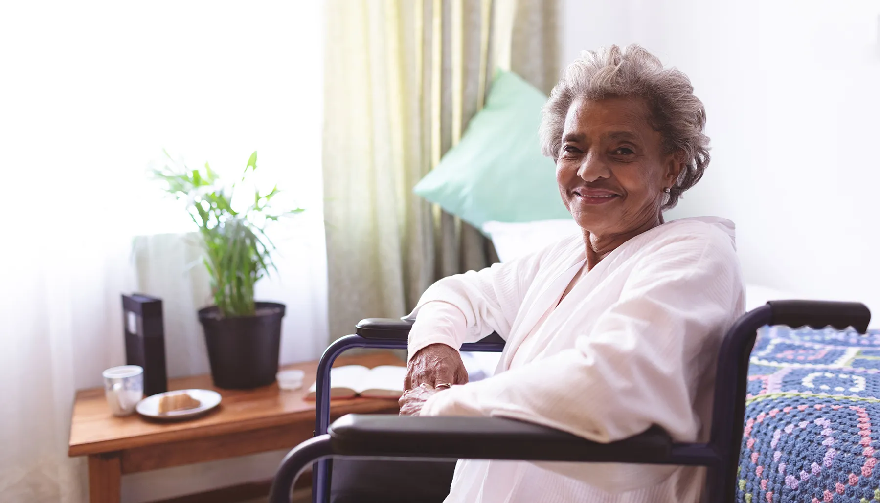 elderly woman sitting in a wheelchair near a window and smiling